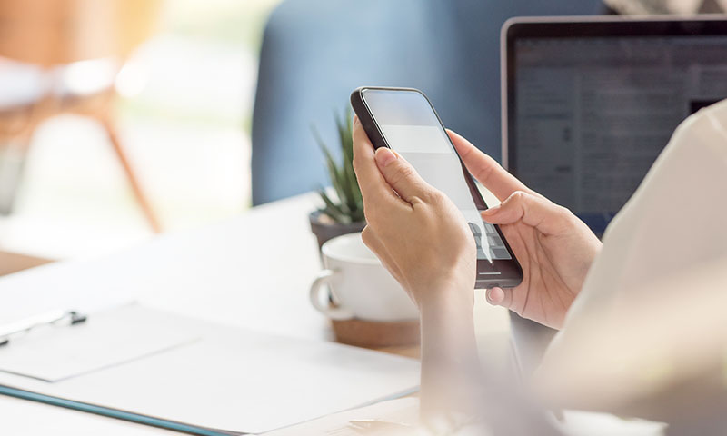 a female using her smart phone and laptop in the background